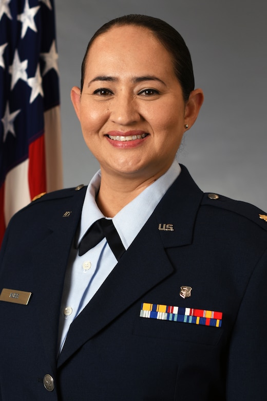An airman in a dress uniform smiles for a photo, with an American flag in the background.