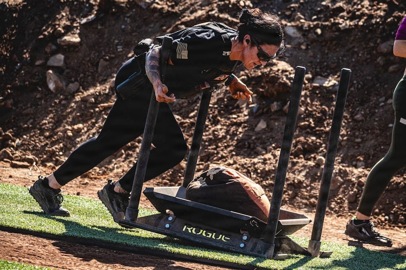 A soldier pushes a metal object down artificial turf.