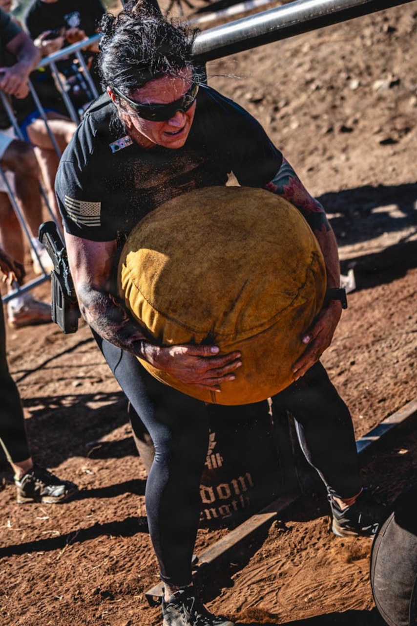 A soldier carries a large ball in muddy terrain.