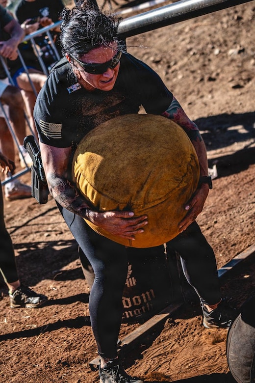 A soldier carries a large ball in muddy terrain.