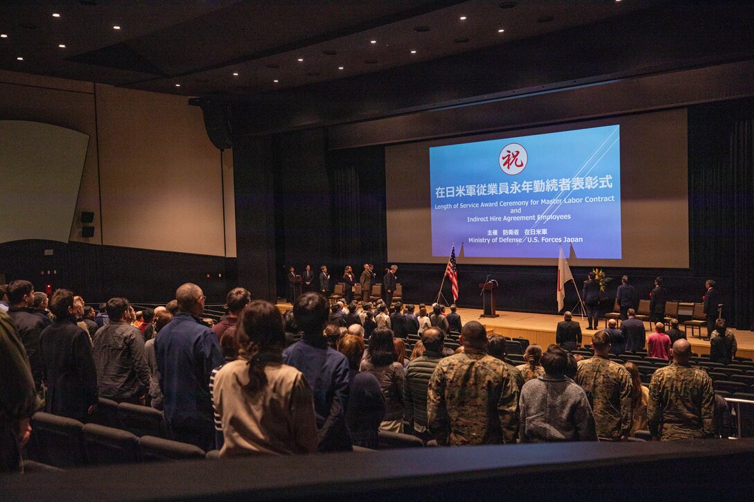 U.S. Marines and Sailors, along with Master Labor Contractors and Indirect Hire Agreement employees stand for the Japanese national anthem during a length of service award ceremony at Marine Corps Air Station Iwakuni, Japan, Jan. 28, 2026. The ceremony celebrates Master Labor Contractors and Indirect Hire Agreement Employees years of service to the air station. (U.S. Marine Corps photo by Lance Cpl. Rylan Adcock)