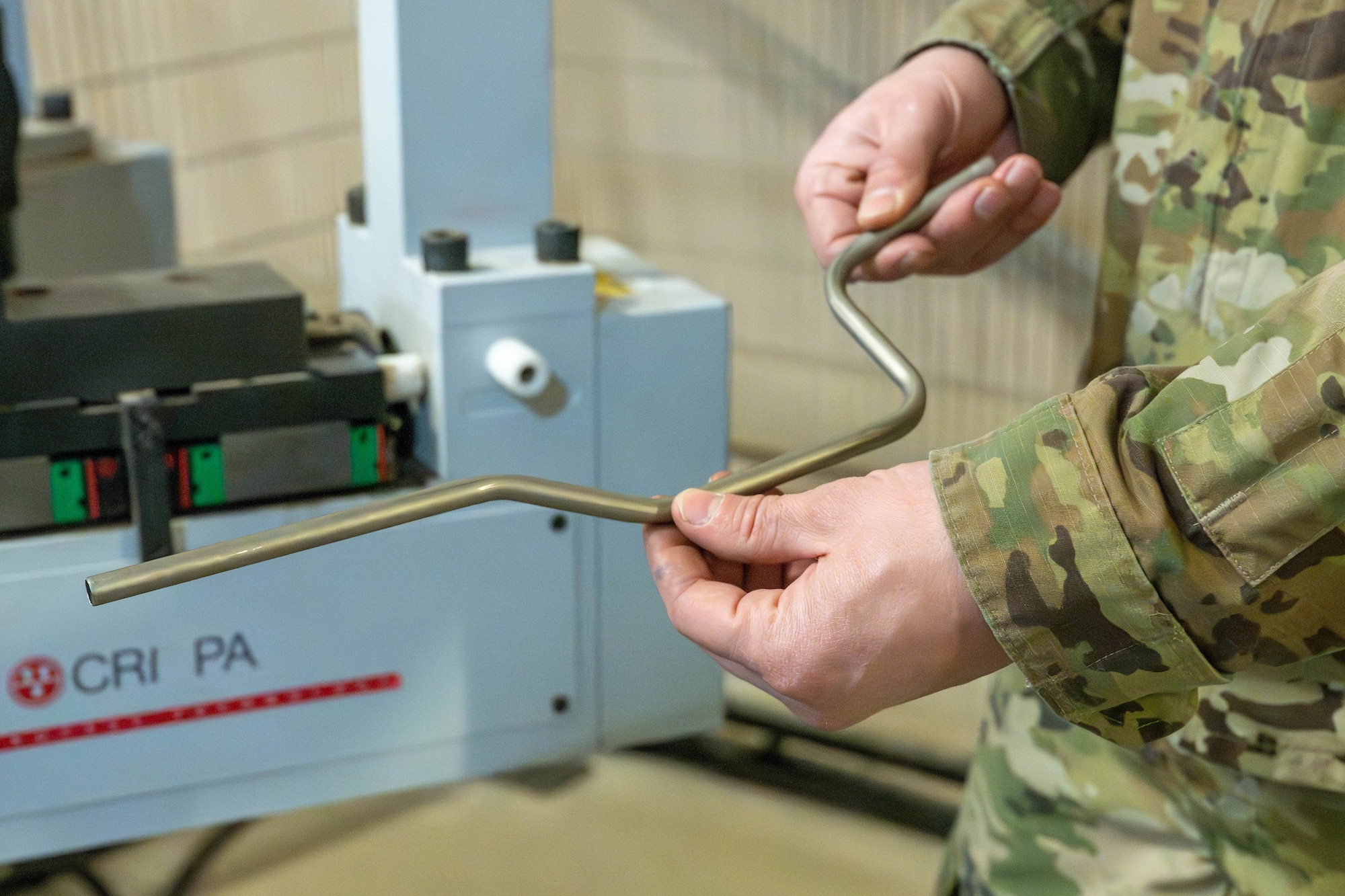 U.S. Air Force Staff Sgt. Matthew McKoin, 332nd Expeditionary Maintenance Squadron aircraft structural maintenance technician, holds a hydraulic line for the main landing gear selector valve of an F-15E Strike Eagle aircraft in the U.S. Central Command area of responsibility, Jan. 28, 2026. The automated system streamlines tube fabrication for aircraft maintenance operations. (U.S. Air Force photo by Senior Airman Kari Degraffenreed)
