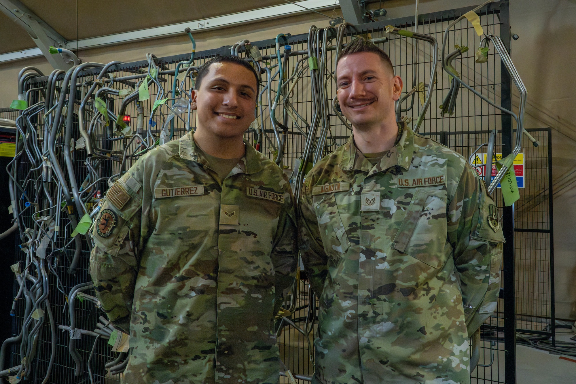 U.S. Air Force Staff Sgt. Matthew McKoin, right, and Airman 1st Class Emmanuel Gutierrez, 332nd Expeditionary Maintenance Squadron aircraft structural maintenance technicians, stand in front of pre-made hydraulic tubes in the U.S. Central Command area of responsibility, Jan. 28, 2026. McKoin and Gutierrez restored a Crippa machine in their shop, improving efficiency and reducing production time. (U.S. Air Force photo by Senior Airman Kari Degraffenreed)