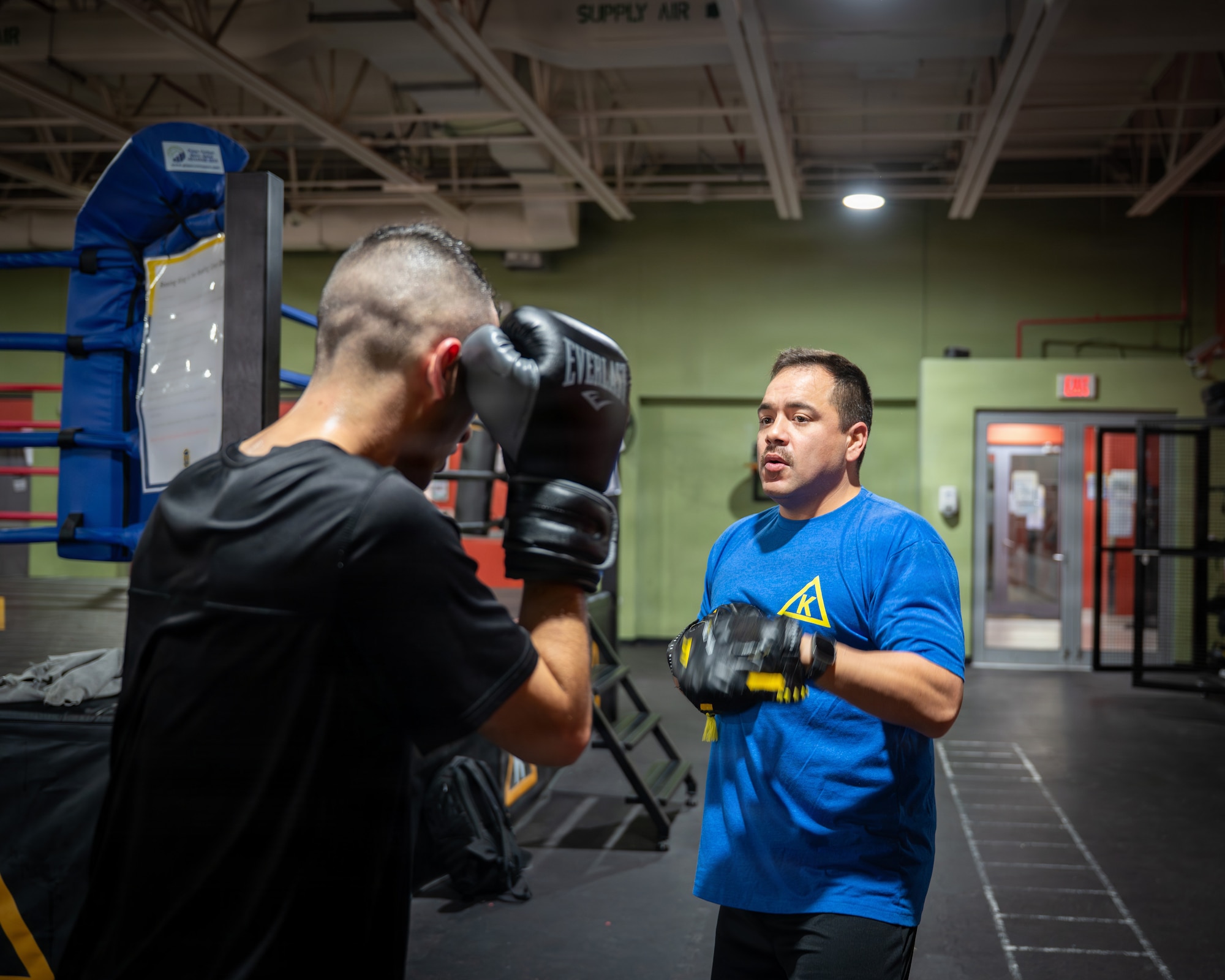 A boxer has his gloves at the ready and a coach is in the middle of bringing his mitts up