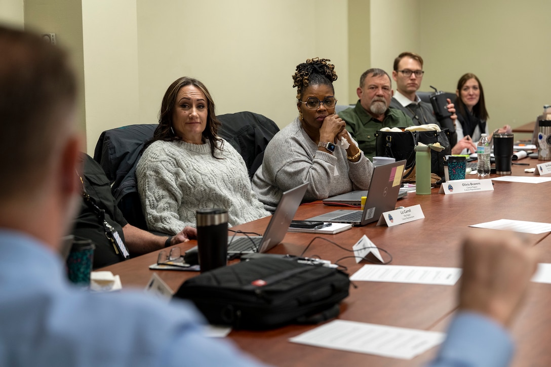 Six people at a conference table talking