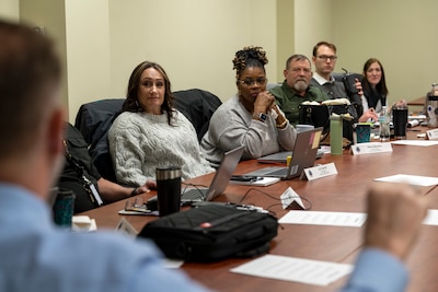 Six people at a conference table talking
