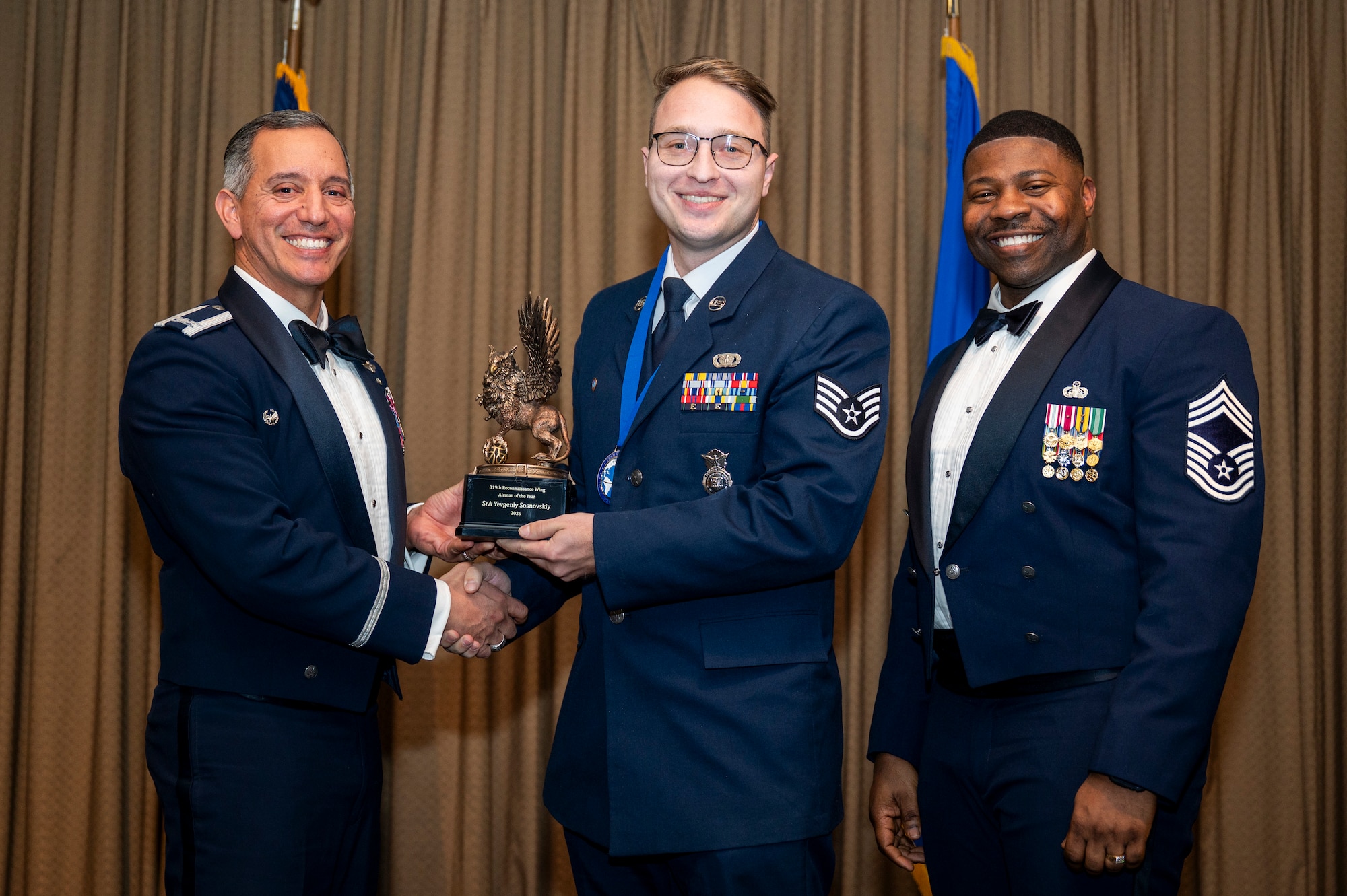 Col. Alfred Rosales, 319th Reconnaissance Wing commander, left and Chief Master Sgt. Marcus Cook Perry, 319th MSG command chief, right, present Taylor R. McGregor, 7th Reconnaissance Squadron, the Airman of the year award during the 319th Reconnaissance Wing’s 2025 annual awards ceremony at Grand Forks Air Force Base, North Dakota, Jan. 29, 2026.