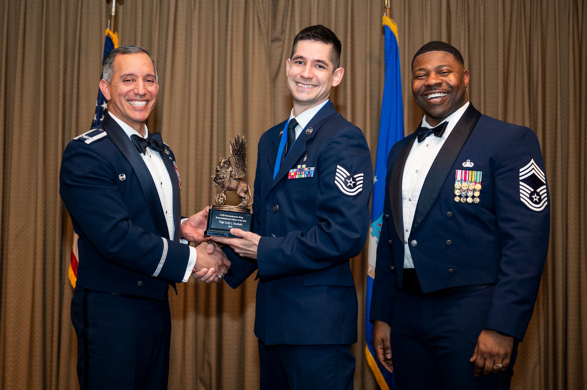 Col. Alfred Rosales, 319th Reconnaissance Wing commander, left and Chief Master Sgt. Marcus Cook Perry, 319th MSG command chief, right, present SSgt Cody J. Duckett, 319th Health Care Operations Squadron, the Non-Commissioned Officer of the year award during the 319th Reconnaissance Wing’s 2025 annual awards ceremony at Grand Forks Air Force Base, North Dakota, Jan. 29, 2026.