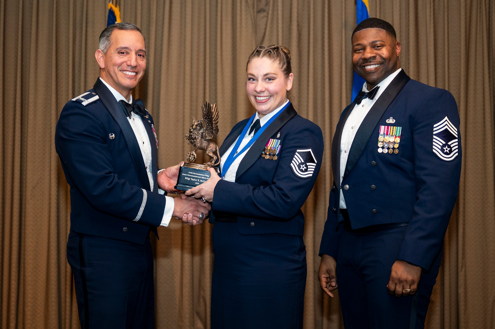 Col. Alfred Rosales, 319th Reconnaissance Wing commander, left and Chief Master Sgt. Marcus Cook Perry, 319th MSG command chief, right, present Taylor R. McGregor, 319th Health Care Operations Squadron, the Senior Non-Commissioned Officer of the year award during the 319th Reconnaissance Wing’s 2025 annual awards ceremony at Grand Forks Air Force Base, North Dakota, Jan. 29, 2026.