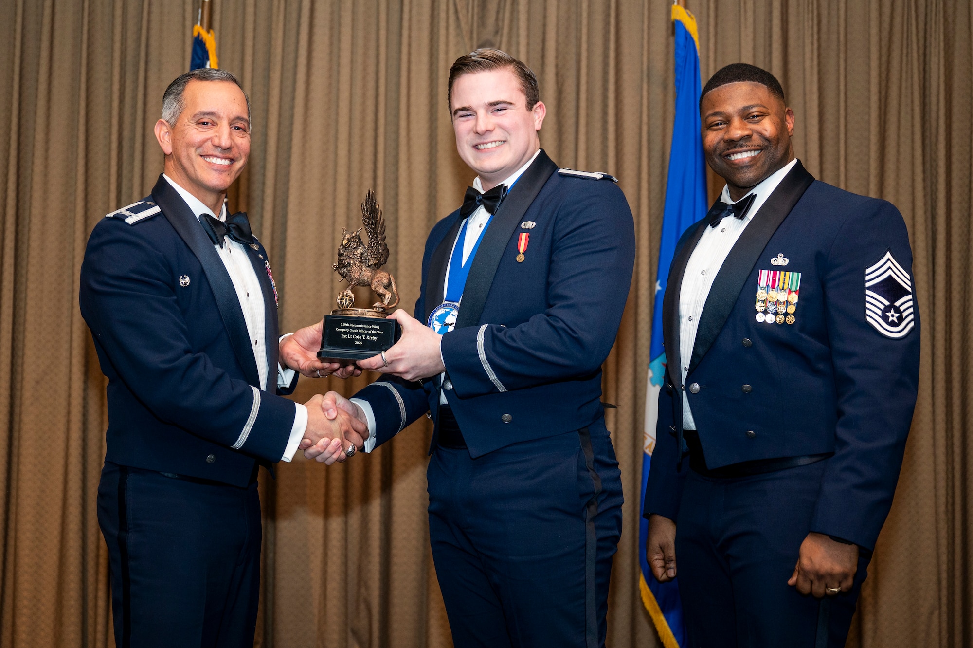 Col. Alfred Rosales, 319th Reconnaissance Wing commander, left and Chief Master Sgt. Marcus Cook Perry, 319th MSG command chief, right, present Lt. Cole T. Kirby, 319th Contracting Squadron, the Company Grade Officer of the year Award, during the 319th Reconnaissance Wing’s 2025 annual awards ceremony at Grand Forks Air Force Base, North Dakota, Jan. 29, 2026.