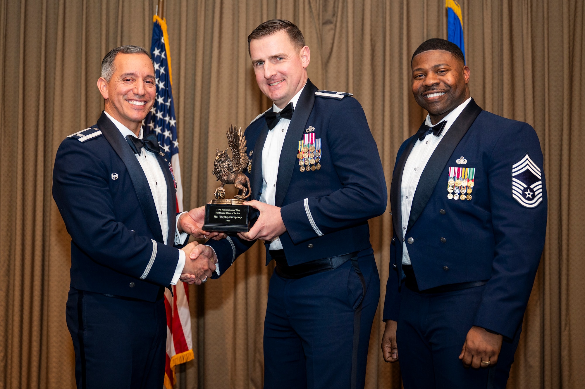 Col. Alfred Rosales, 319th Reconnaissance Wing commander, left and Chief Master Sgt. Marcus Cook Perry, 319th MSG command chief, right, present Maj. Joseph J. Humphrey, Civil Engineer Squadron, the Field Grade Officer of the year award during the 319th Reconnaissance Wing’s 2025 annual awards ceremony at Grand Forks Air Force Base, North Dakota, Jan. 29, 2026.