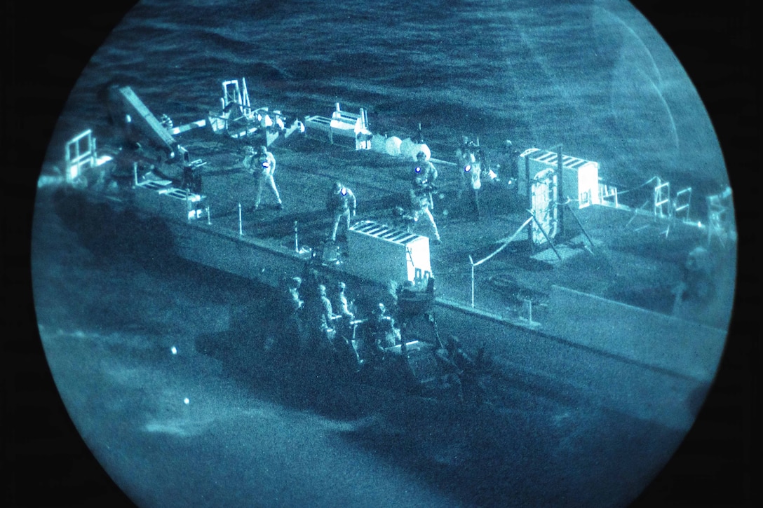 Marines on a boat prepare to board a ship in a body of water as seen through a night vision lens.