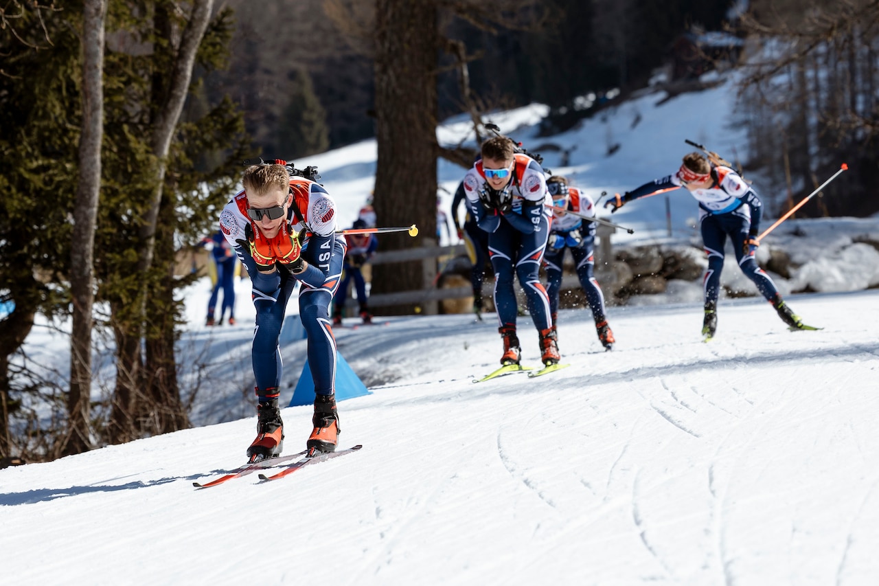 A man wearing sports attire hunches low on skis while leading a pack of racers down a snowy hill.