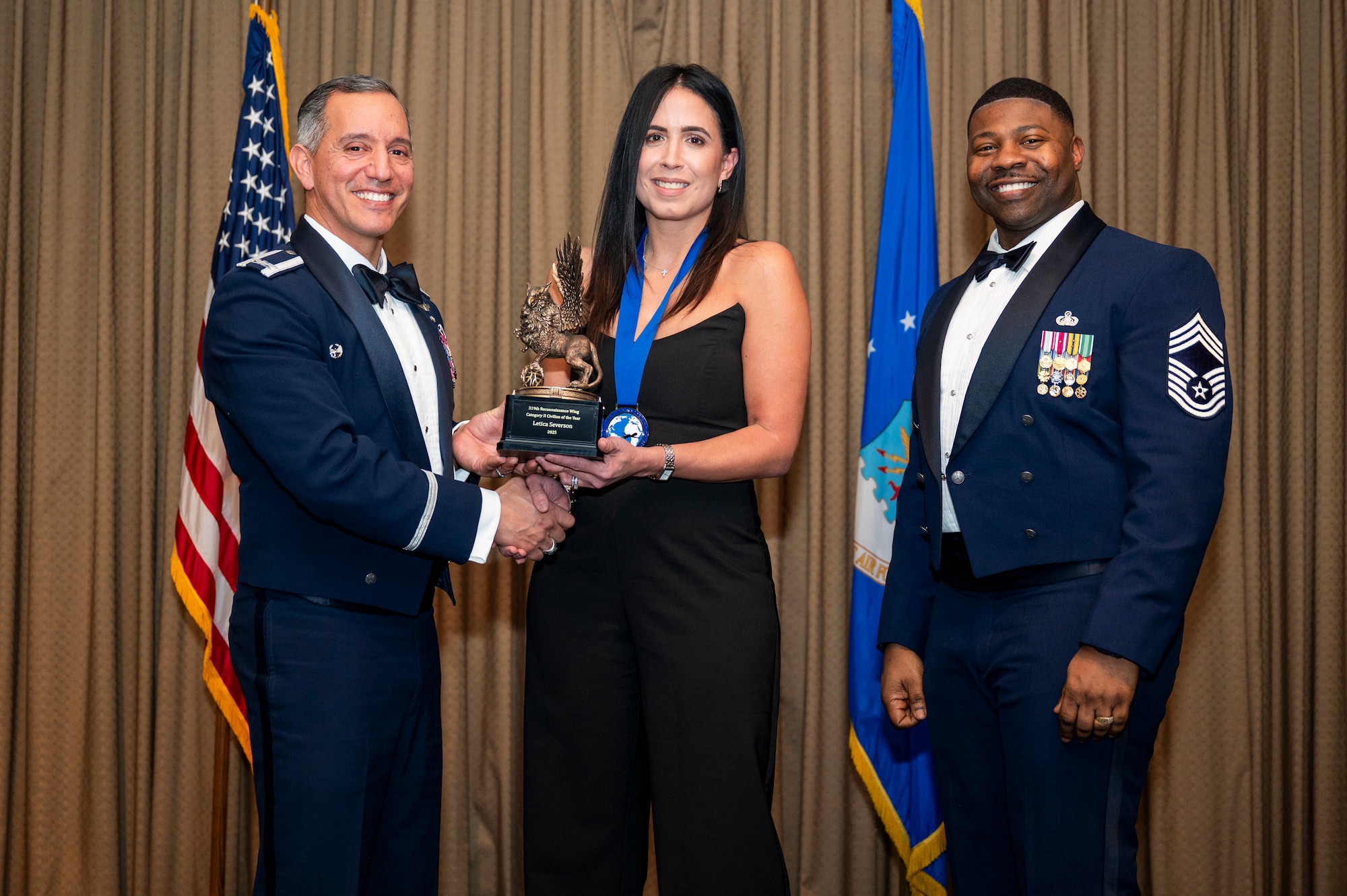 Col. Alfred Rosales, 319th Reconnaissance Wing commander, left and Chief Master Sgt. Marcus Cook Perry, 319th MSG command chief, right, present Letica Severson, 319th Operations Group, the Category II Civilian of the year award during the 319th Reconnaissance Wing’s 2025 annual awards ceremony at Grand Forks Air Force Base, North Dakota, Jan. 29, 2026
