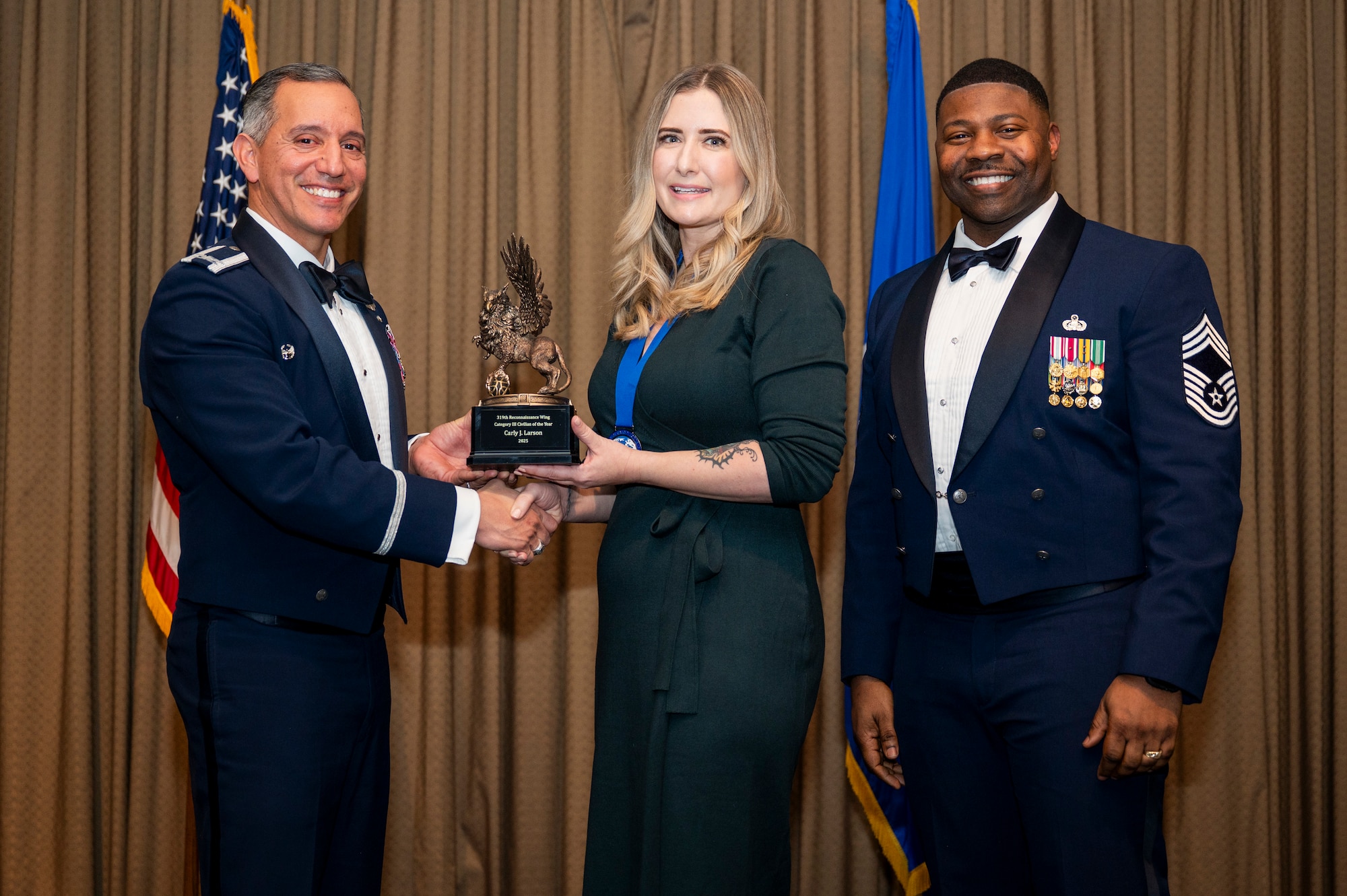 Col. Alfred Rosales, 319th Reconnaissance Wing commander, left and Chief Master Sgt. Marcus Cook Perry, 319th MSG command chief, right, present Carly J. Larson, 319th Contracting Squadron, the Civilian Category III of the year award during the 319th Reconnaissance Wing’s 2025 annual awards ceremony at Grand Forks Air Force Base, North Dakota, Jan. 29, 2026.