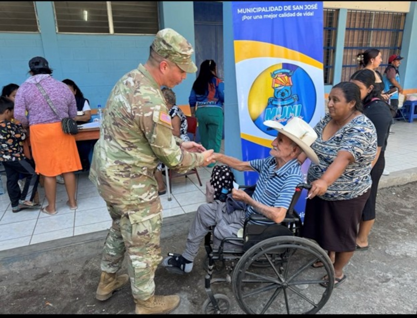 A soldier wearing a military uniform shakes the hand of a person in a wheel chair