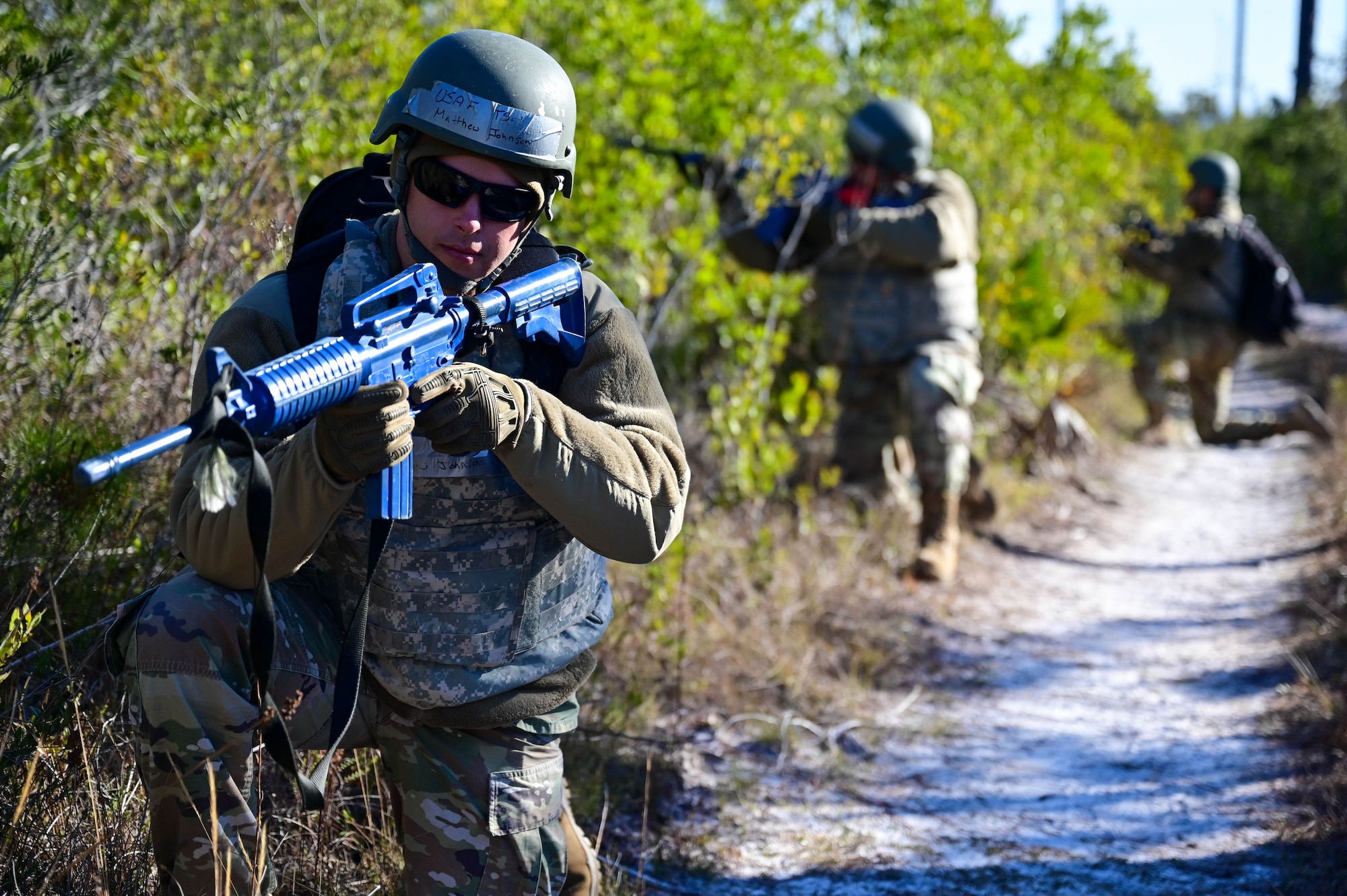 Three Airmen crouch in the sand with fake guns.