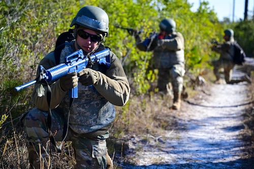 Three Airmen crouch in the sand with fake guns.