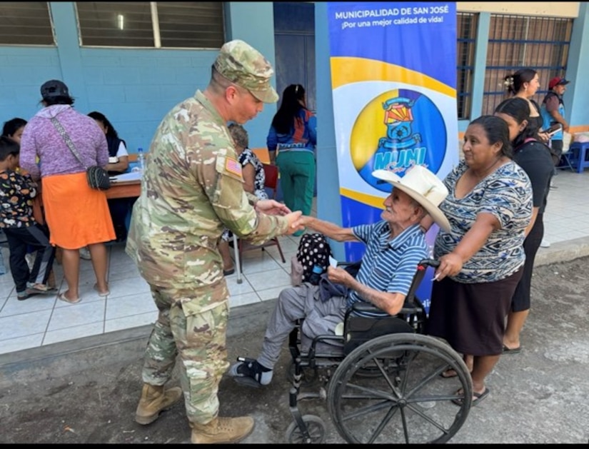 A soldier wearing a military uniform shakes the hand of a person in a wheel chair