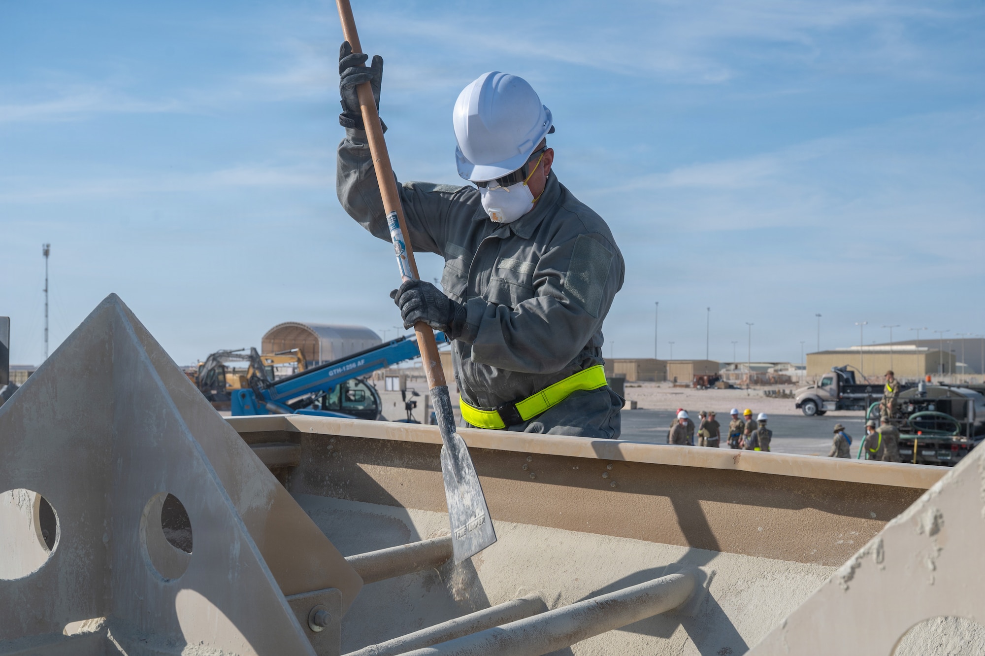 An Airman uses a tool to mix fill material in a large container