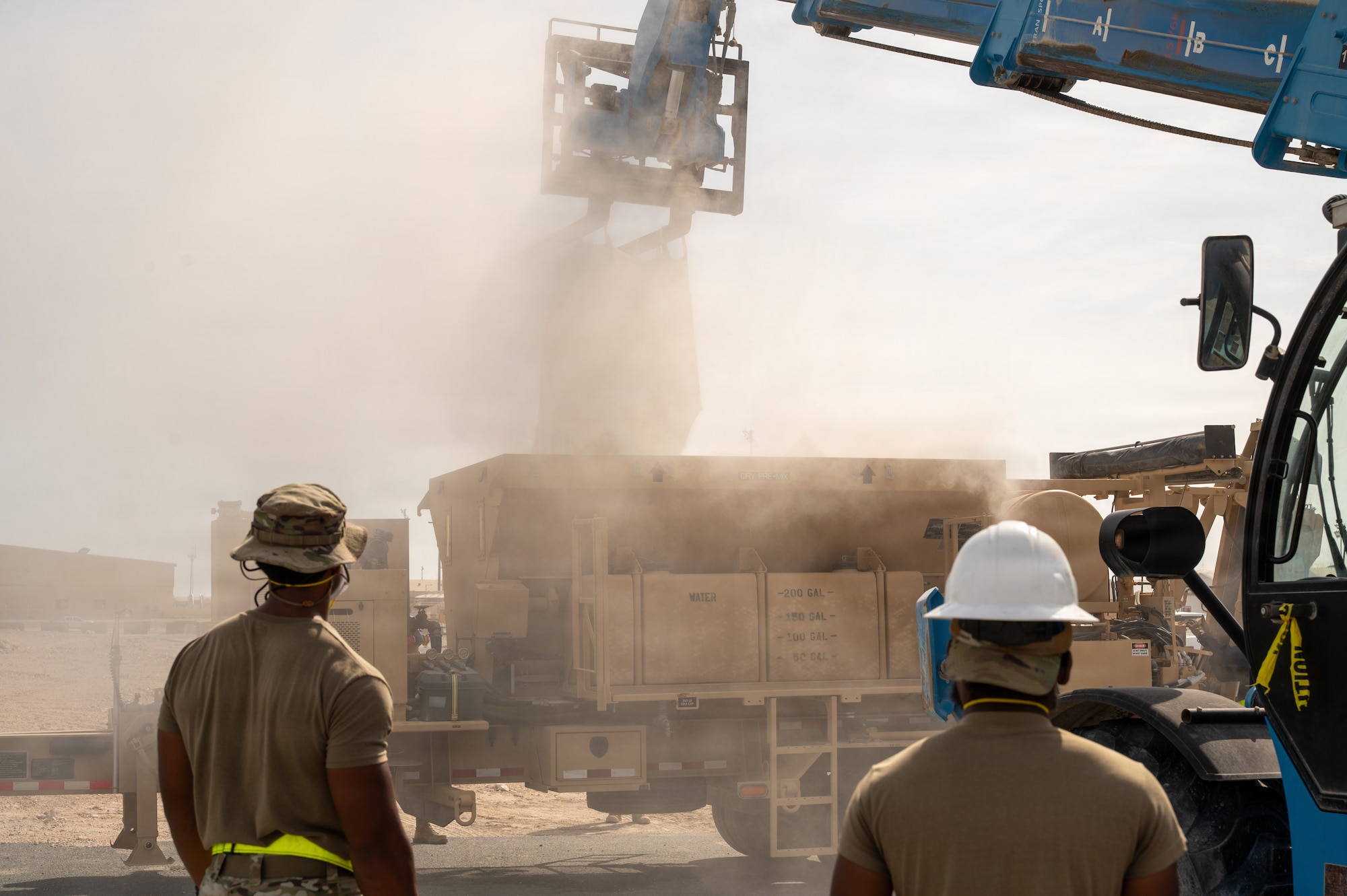 Two Airmen in the foreground look on as a forklift lifts an indiscernible object out of a large truck