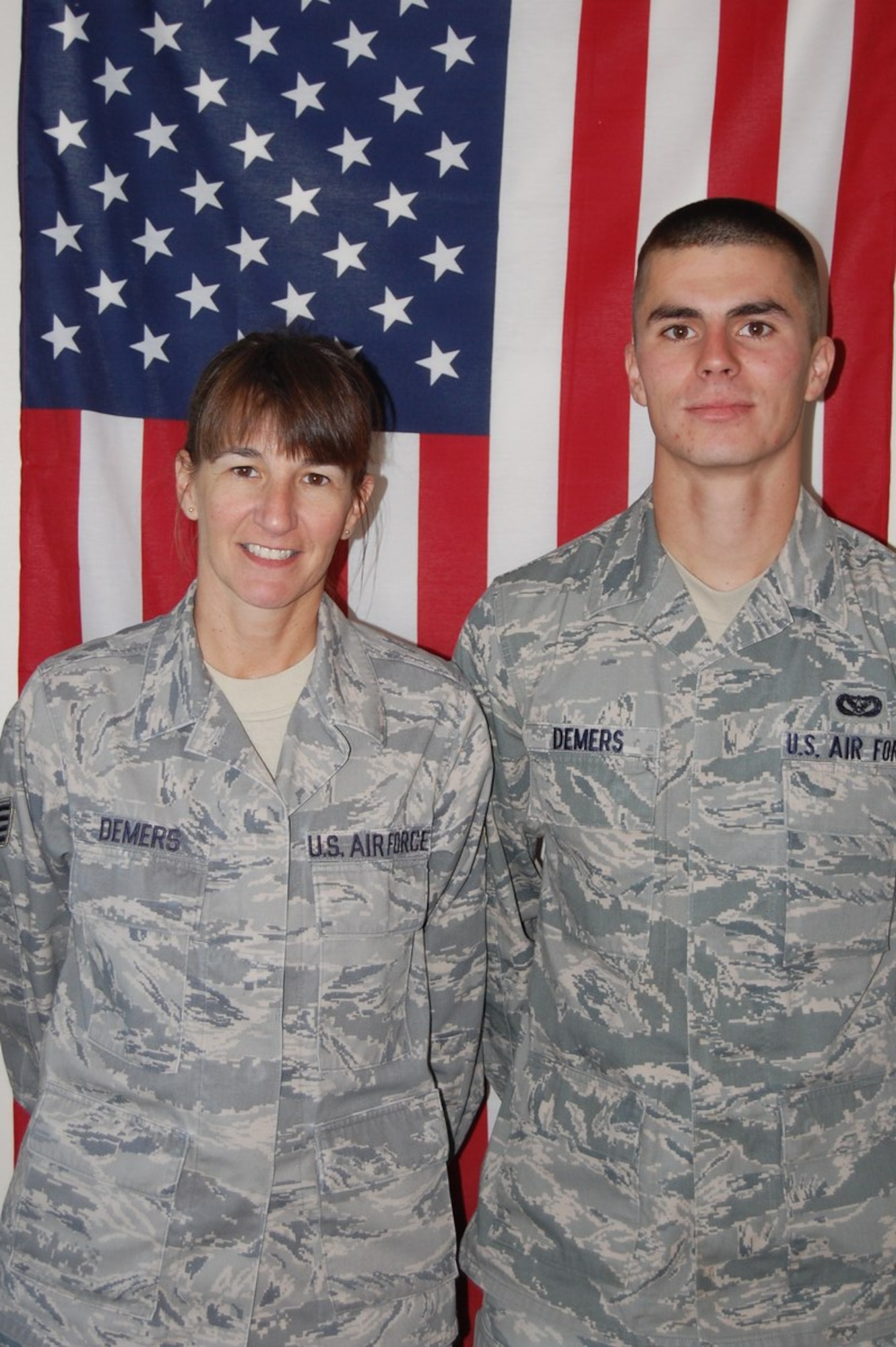 Mother and son stand next to each other in front of a flag