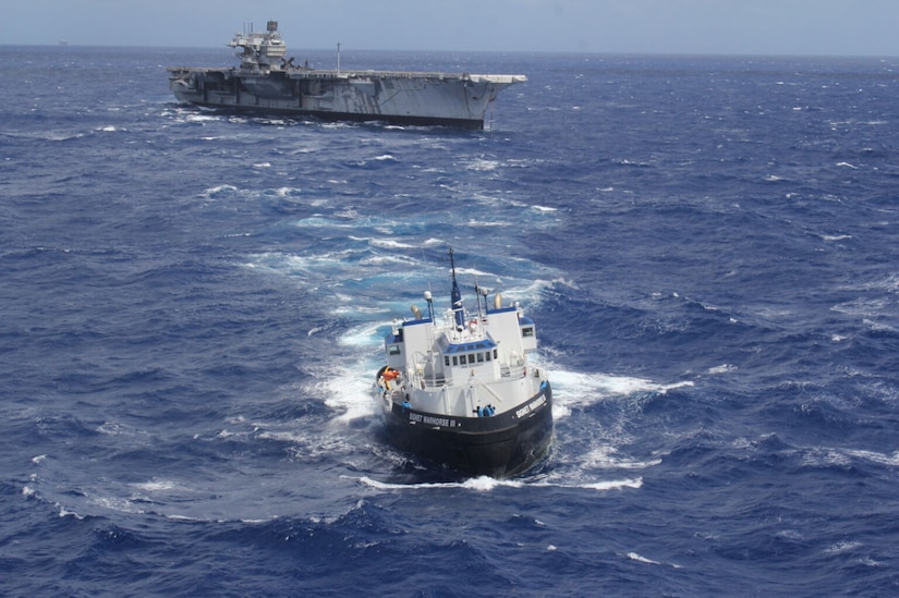A tugboat tows an aircraft carrier at sea.