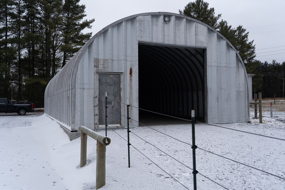 A snowy scene showcases an arched metal building used as a horse barn. Fencing and associated structures surround the building.