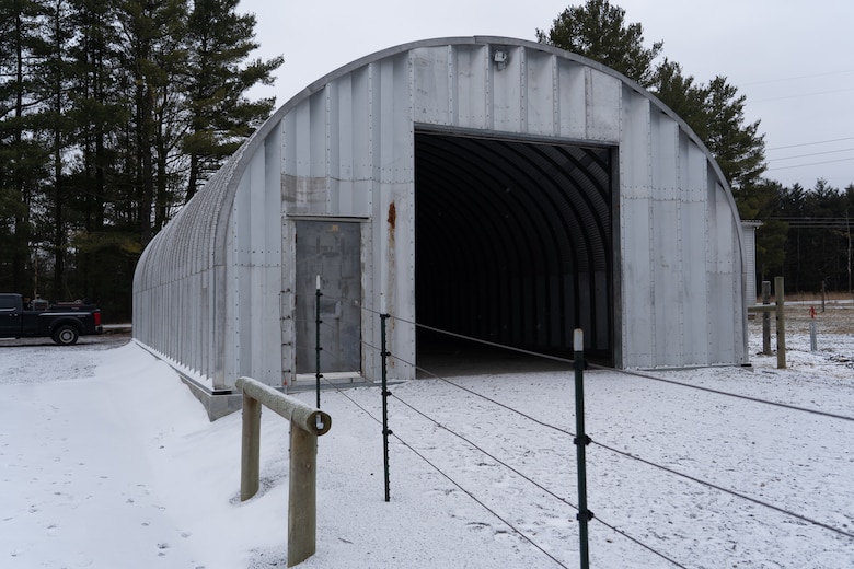 A snowy scene showcases an arched metal building used as a horse barn. Fencing and associated structures surround the building.