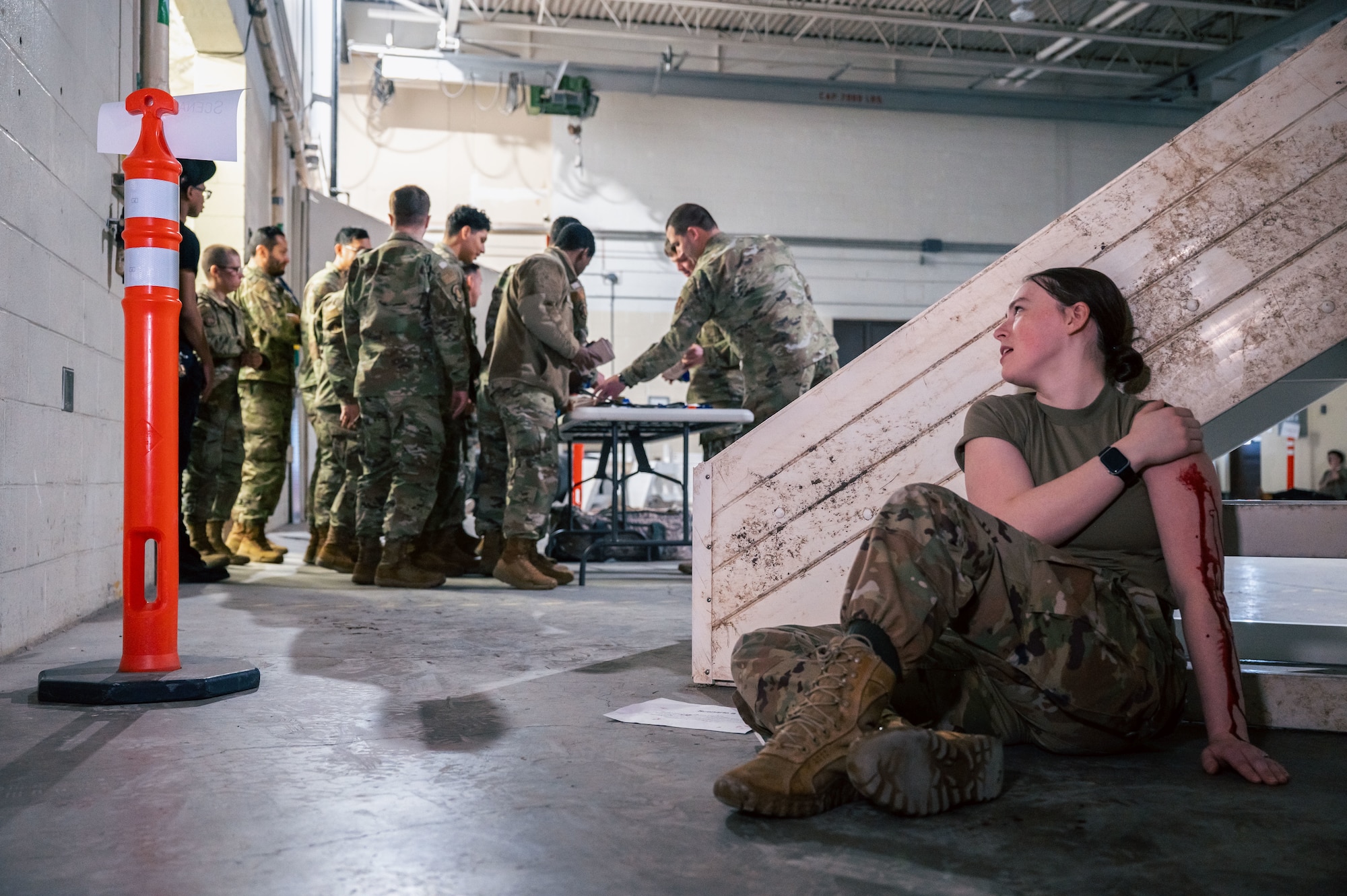 Woman in uniform up against a structure with many service members in the background