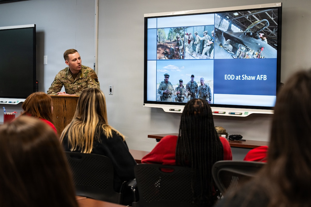 An Airman shows a presentation on a digital whiteboard to students in a classroom