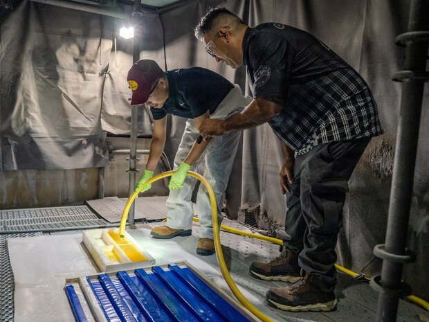 King Joash (KJ) Rumbaoa, a student from the University of Hawaii Manoa, pours Versathane, a urethane resin, into molds under the watchful eye of Dean Tamaki, a painter at Pearl Harbor Naval Shipyard and Intermediate Maintenance Facility, on Oct. 24, 2025.