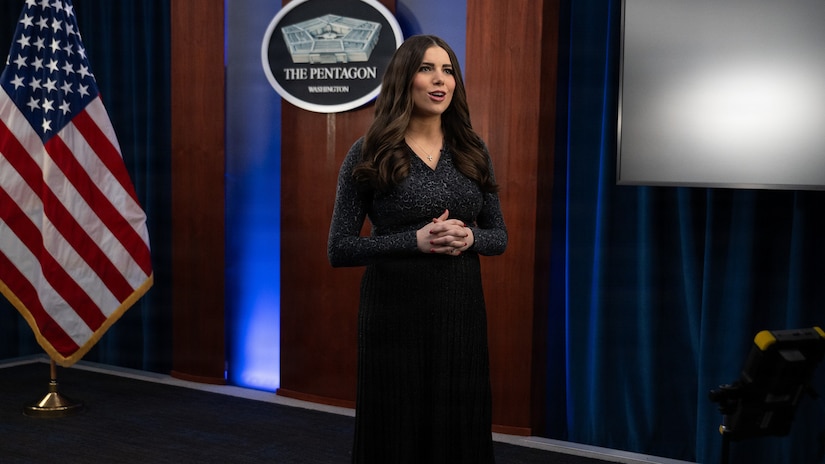 The Pentagon press secretary delivers remarks against a blue background with an American flag on the left.