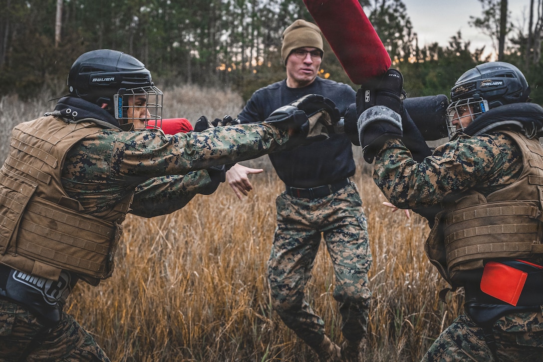 A Marine watches as two Marines compete with pugil sticks in a field.