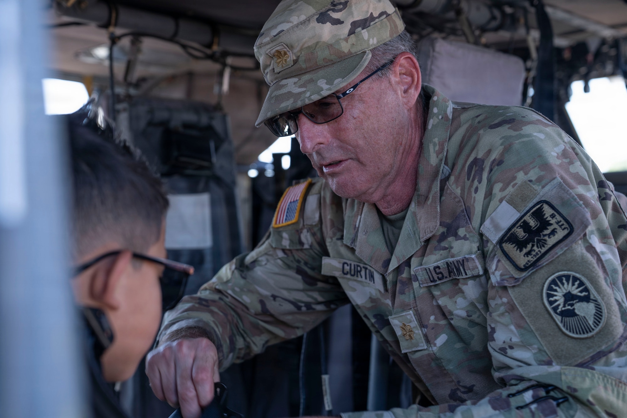 A person in a military uniform helps buckle a child into a seat of a helicopter