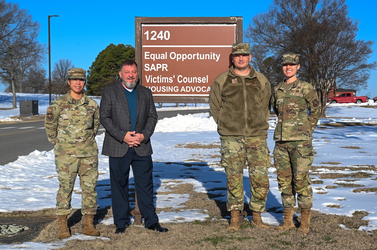 Service members stand in front of building sign.