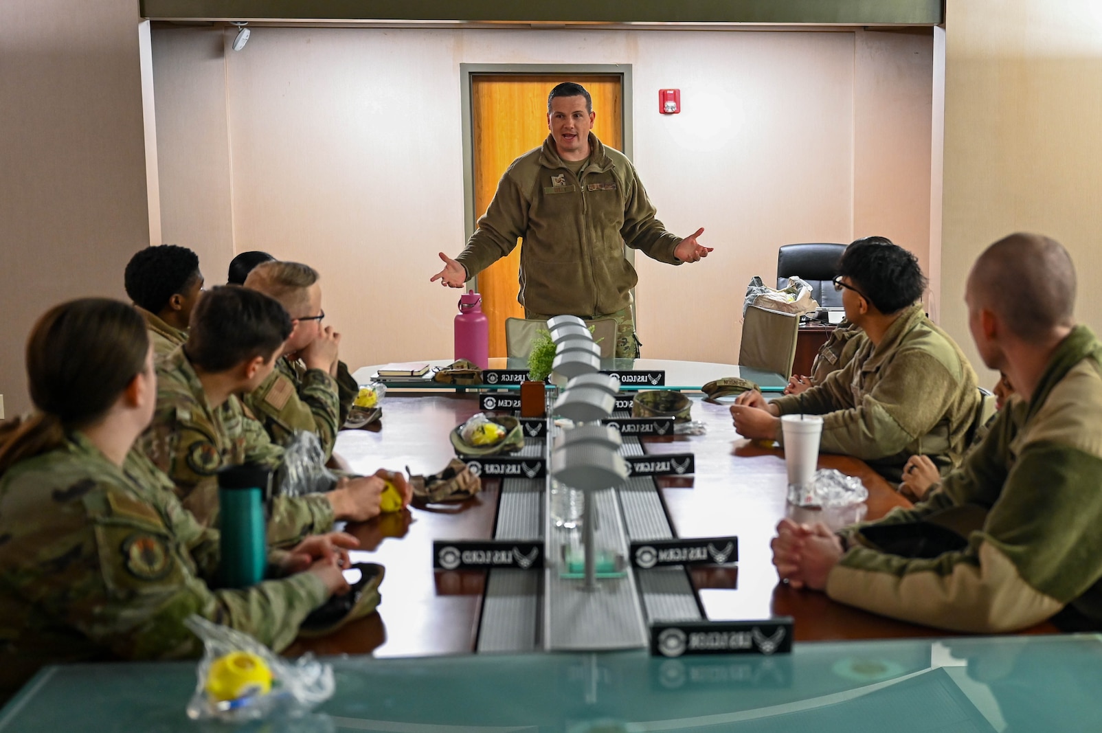 A man stands and talks to table people sitting around a table.
