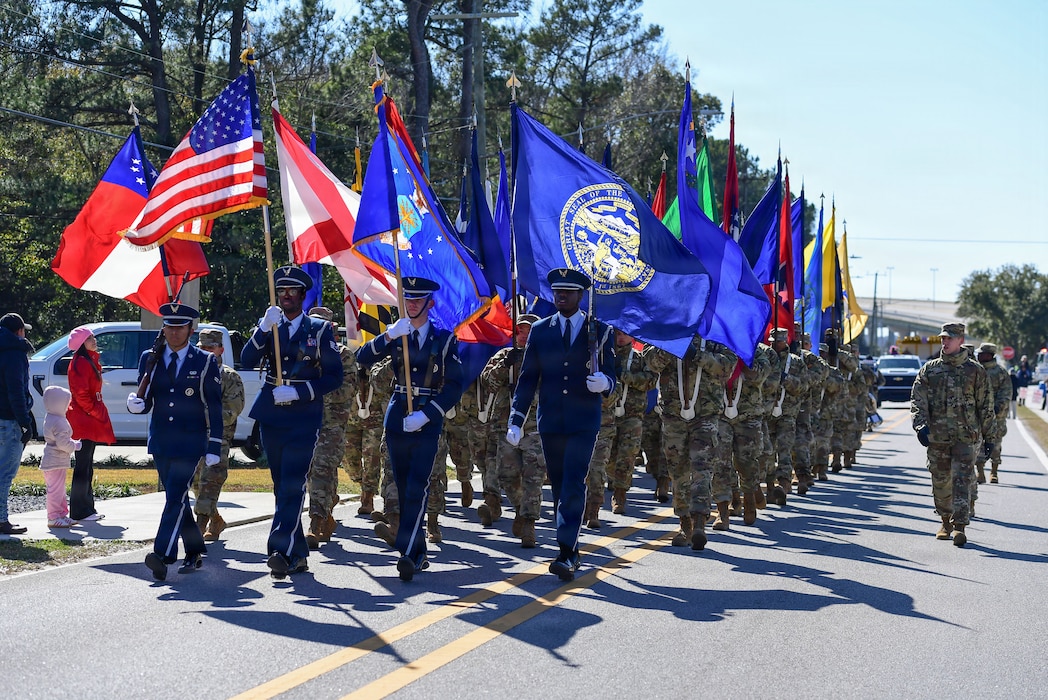 U.S. Airmen in military uniforms walk through the streets carrying the American Flag and U.S. State Flags.
