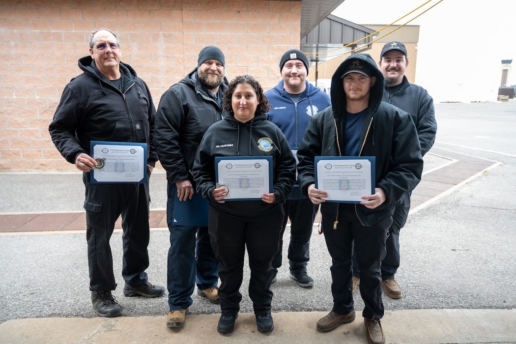U.S. Air Force 97th Aircraft Maintenance Squadron members pose with Knuckle Buster certificates at Altus Air Force Base, Oklahoma, Jan. 22, 2026. The maintainers were given Knuckle Buster awards for performing above-standard field work on repairing a KC-135 Stratotanker aircraft trunnion, a critical part of the landing gear. (U.S. Air Force photo by Airman 1st Class Nathan Langston)