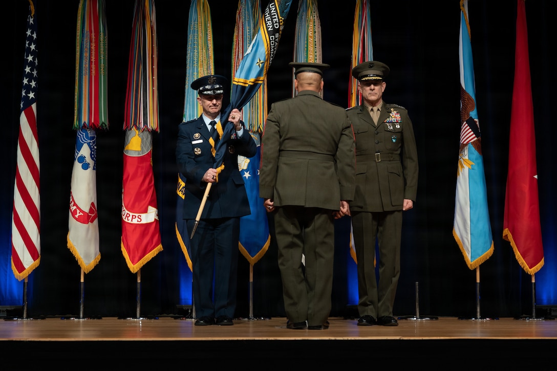 Men in dress military uniforms salute each other on a stage.