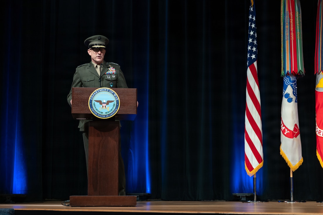 A man in an olive colored military uniform speaks at a podium.