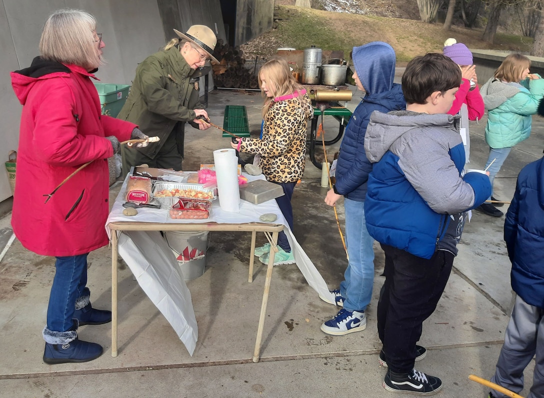 Photo of Libby Dam Park Ranger Susan James distributing marshmallows to elementary school-aged students to make s'mores, during the Friends of Scotchman Peak’s 12th annual “Winter Tracks” event, Jan. 23, 2026 and Jan 29, 2026. Libby Dam, a U.S. Army Corps of Engineers' operating project in Libby, Montana, hosted this year's event.