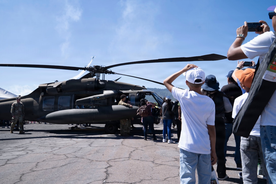 People stand in line outside of a military helicopter.