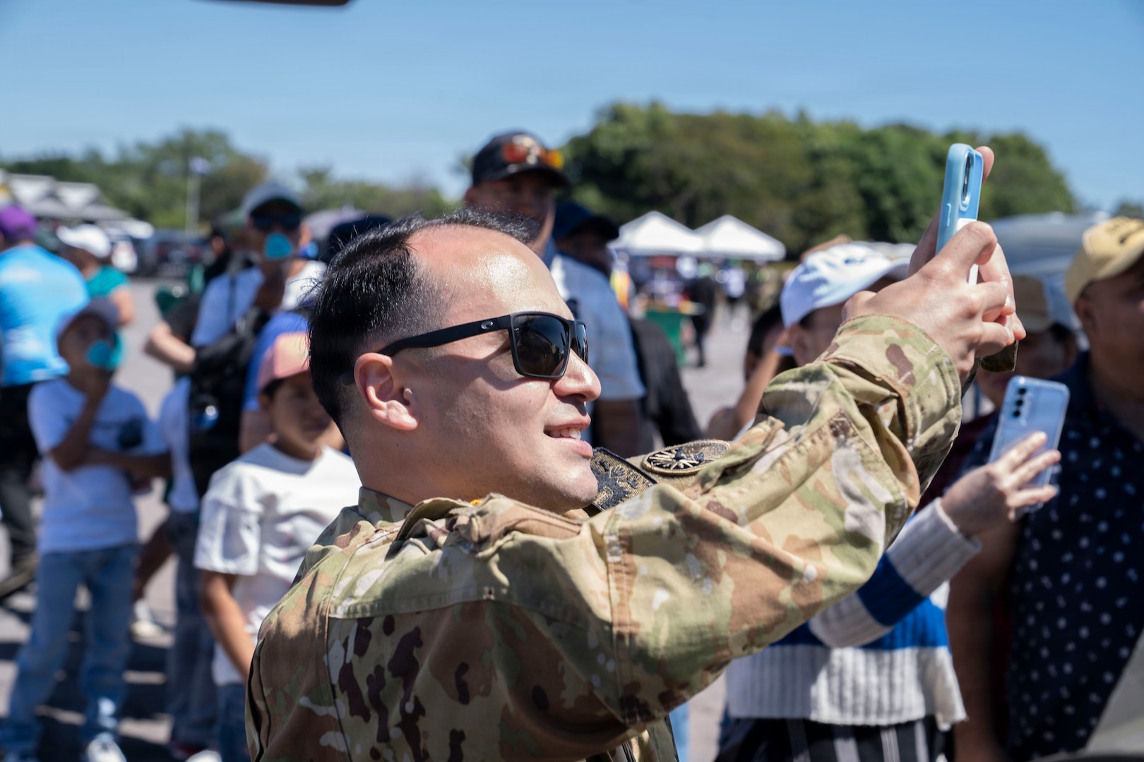 A person in military clothing takes a picture on a cell phone.