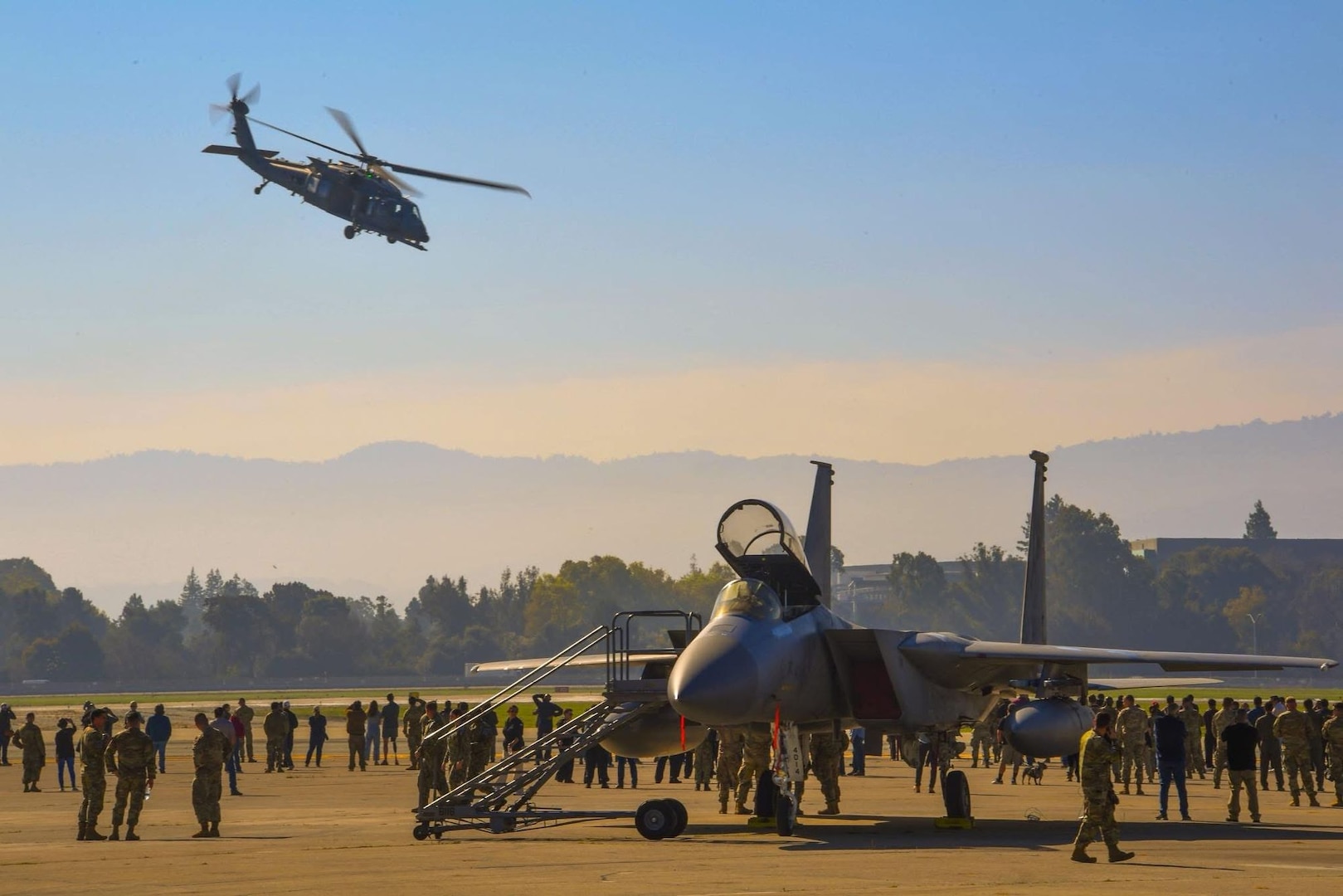Community members watch a rescue demonstration as an HH-60W Jolly Green II helicopter from the 129th Rescue Wing, California Air National Guard, flies overhead while aircraft performing the Super Bowl LX flyover – including an F-15C Eagle from the 144th Fighter Wing – are on static display, Feb. 5, at Moffett Air National Guard Base, Calif.