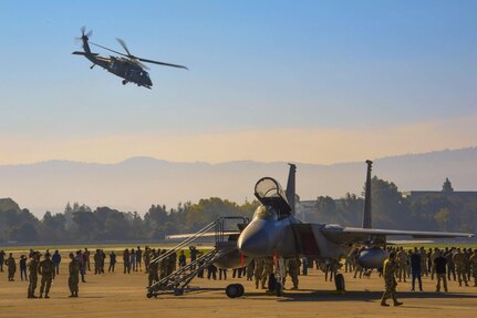 Community members watch a rescue demonstration as an HH-60W Jolly Green II helicopter from the 129th Rescue Wing, California Air National Guard, flies overhead while aircraft performing the Super Bowl LX flyover – including an F-15C Eagle from the 144th Fighter Wing – are on static display, Feb. 5, at Moffett Air National Guard Base, Calif.