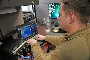 an Airman looks at a laptop featuring a map while typing