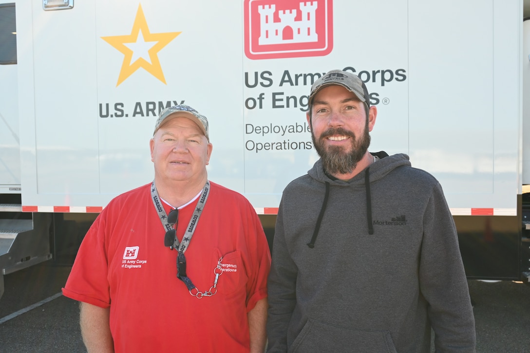 Two men stand in front of a large vehicle.