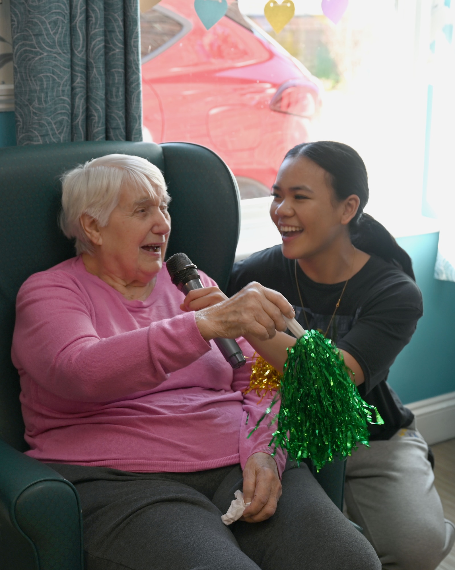 U.S. Air Force Senior Airman Angeryll Tipay, 100th Civil Engineer Squadron sings karaoke with a resident at Mabbs Hall Care Home, Mildenhall, England, Jan. 28, 2026. Airmen with the RAF Mildenhall Top 3, 100th CES and 100th Communications Squadron visited the local care home to spend time with and entertain residents. (U.S. Air Force photo by Karen Abeyasekere)