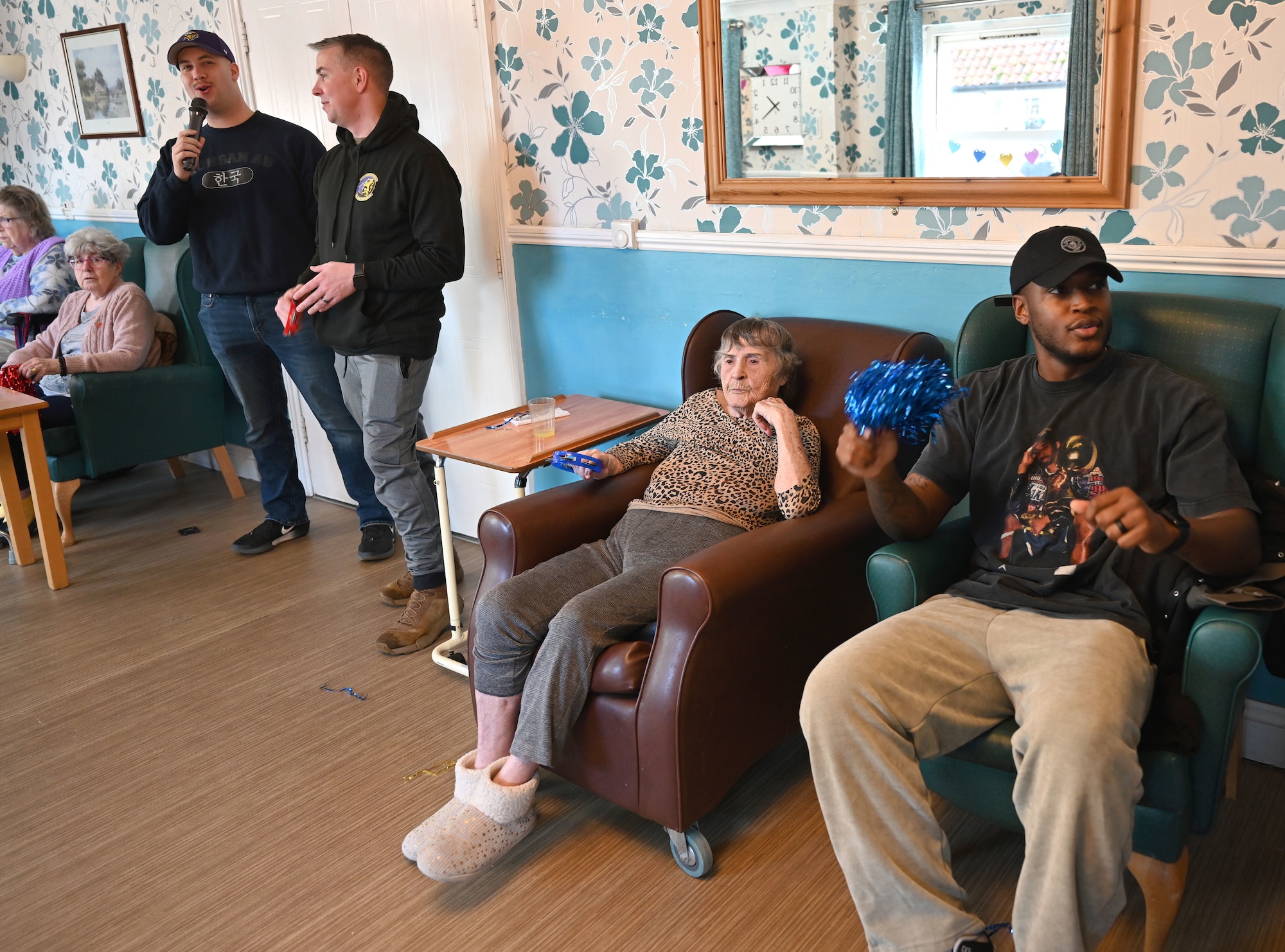 From left, U.S. Air Force Staff Sgt. Justin Bosch, Master Sgt. Jamie Fewin and Staff Sgt. Clarence Burnett, all 100th Civil Engineer Squadron Airmen, sing karaoke to entertain residents at Mabbs Hall Care Home, Mildenhall, England, Jan. 28, 2026. Airmen with the RAF Mildenhall Top 3, 100th CES and 100th Communications Squadron visited the local care home to spend time with and entertain residents. Team Mildenhall Airmen regularly volunteer within the local area to strengthen partnerships and build community relations. (U.S. Air Force photo by Karen Abeyasekere)